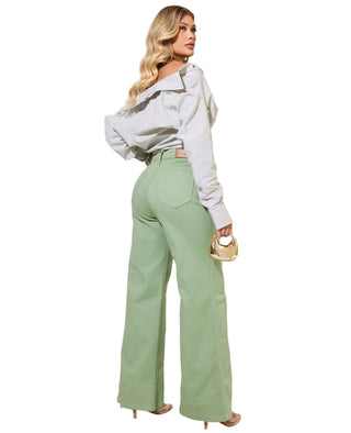 Woman wearing a light gray off-shoulder top and green pants standing indoors.